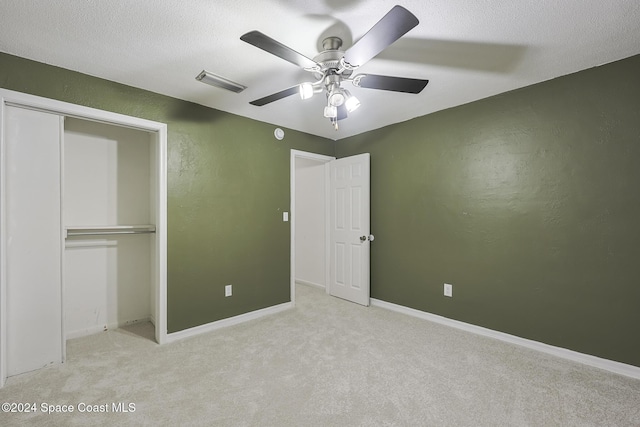 unfurnished bedroom with ceiling fan, light colored carpet, a textured ceiling, and a closet