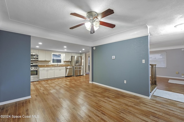 kitchen featuring ceiling fan, sink, appliances with stainless steel finishes, white cabinets, and light wood-type flooring