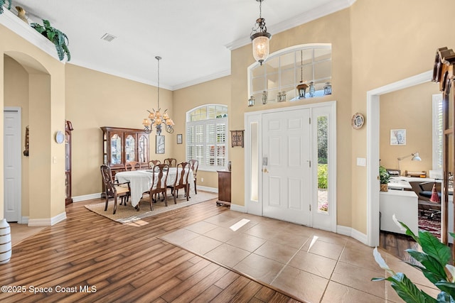 foyer entrance with crown molding, a towering ceiling, wood-type flooring, and an inviting chandelier