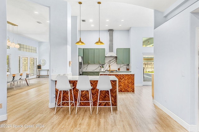 kitchen with a kitchen bar, kitchen peninsula, wall chimney range hood, stainless steel refrigerator, and green cabinets