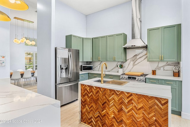 kitchen with wall chimney range hood, sink, hanging light fixtures, light stone countertops, and stainless steel appliances