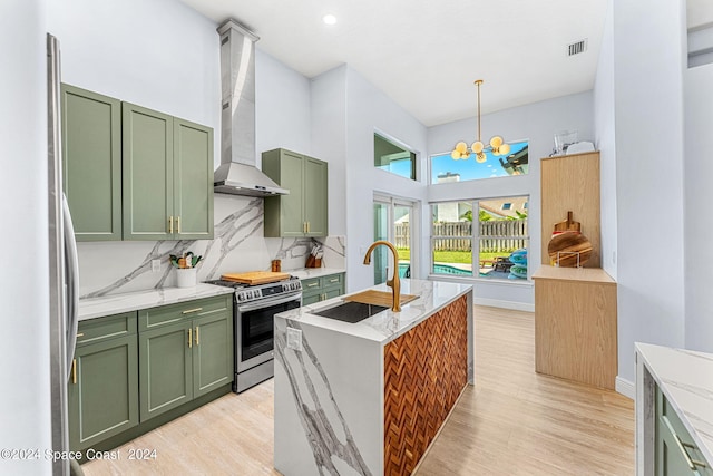 kitchen featuring backsplash, green cabinets, wall chimney range hood, sink, and appliances with stainless steel finishes