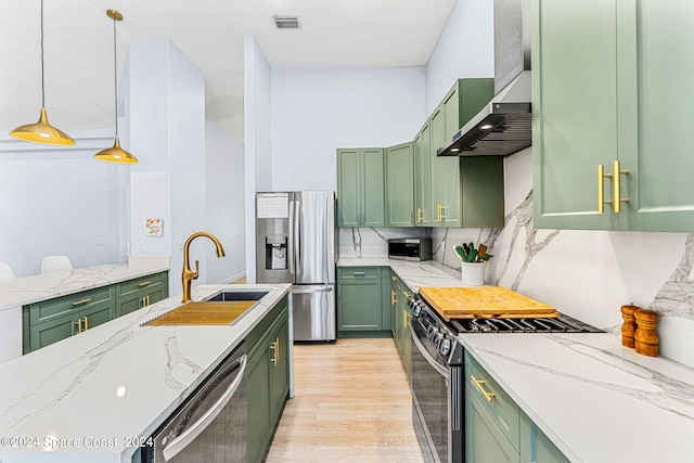 kitchen featuring wall chimney exhaust hood, stainless steel appliances, sink, pendant lighting, and green cabinets