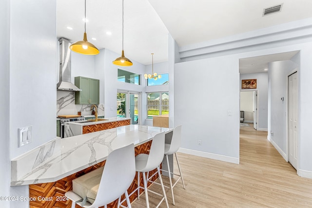 kitchen with a kitchen bar, decorative light fixtures, green cabinets, and wall chimney range hood