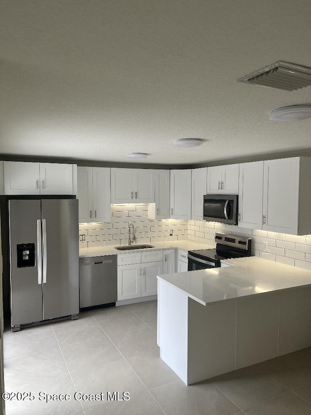 kitchen with kitchen peninsula, light tile patterned floors, white cabinets, appliances with stainless steel finishes, and sink