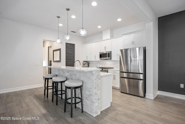 kitchen with appliances with stainless steel finishes, light wood-type flooring, pendant lighting, a center island with sink, and white cabinets