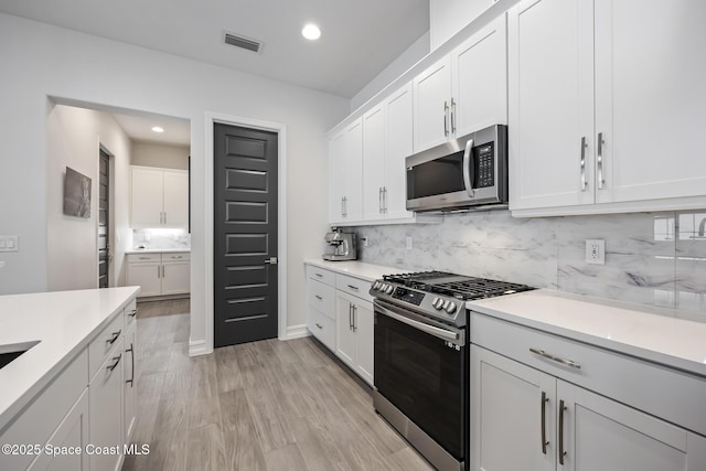 kitchen with white cabinets, light hardwood / wood-style floors, stainless steel appliances, and tasteful backsplash