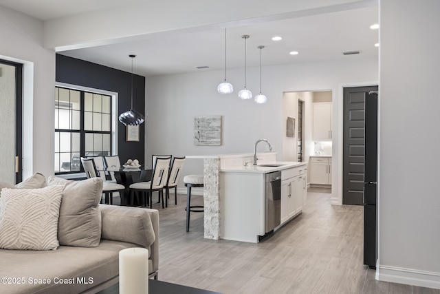 kitchen featuring a kitchen island with sink, sink, decorative light fixtures, dishwasher, and white cabinetry