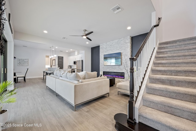 living room featuring ceiling fan, a stone fireplace, and light hardwood / wood-style flooring