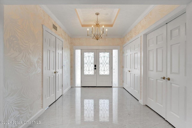 foyer featuring a raised ceiling, french doors, a chandelier, and ornamental molding