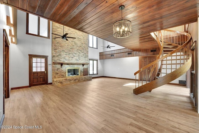 unfurnished living room with wooden ceiling, a brick fireplace, a towering ceiling, ceiling fan with notable chandelier, and light wood-type flooring