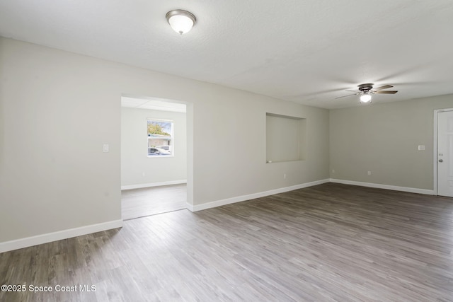 empty room featuring ceiling fan, a textured ceiling, baseboards, and wood finished floors