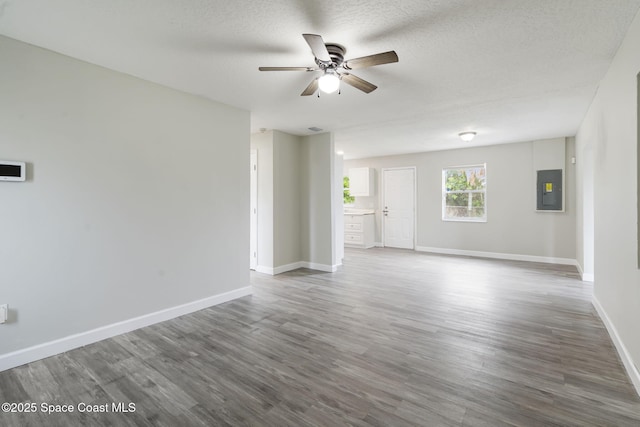 unfurnished living room featuring electric panel, baseboards, a textured ceiling, and wood finished floors