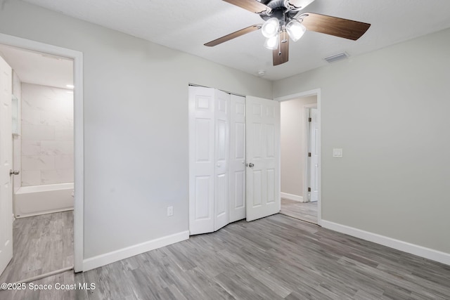 unfurnished bedroom with wood finished floors, visible vents, baseboards, a closet, and connected bathroom