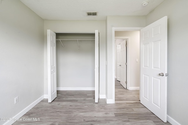 unfurnished bedroom featuring wood finished floors, baseboards, visible vents, and a closet