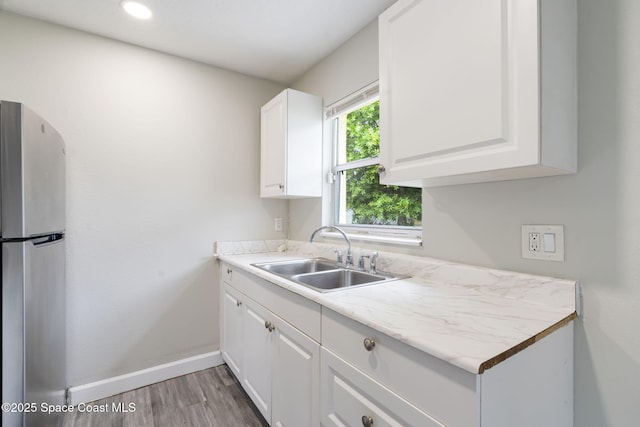 kitchen featuring baseboards, freestanding refrigerator, a sink, light countertops, and white cabinets