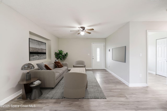 living room featuring light wood finished floors, a ceiling fan, and baseboards