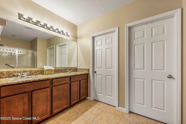 bathroom with tile patterned floors, vanity, a shower with shower door, and a textured ceiling