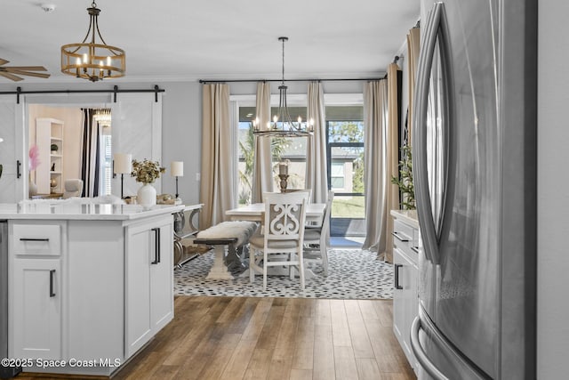 kitchen featuring crown molding, pendant lighting, a barn door, white cabinetry, and stainless steel refrigerator