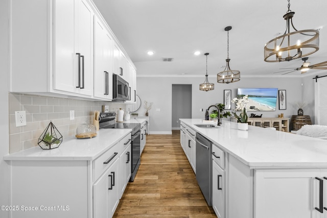 kitchen with sink, pendant lighting, a kitchen island with sink, white cabinets, and appliances with stainless steel finishes