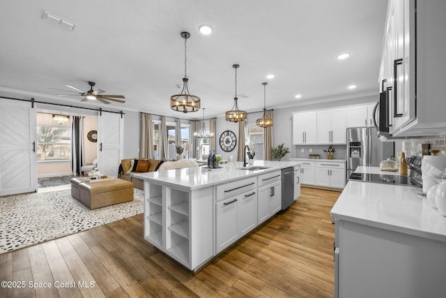 kitchen with a center island with sink, sink, a barn door, decorative light fixtures, and white cabinetry