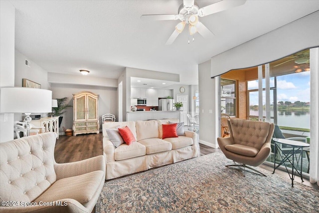 living room featuring ceiling fan, a water view, and dark wood-type flooring