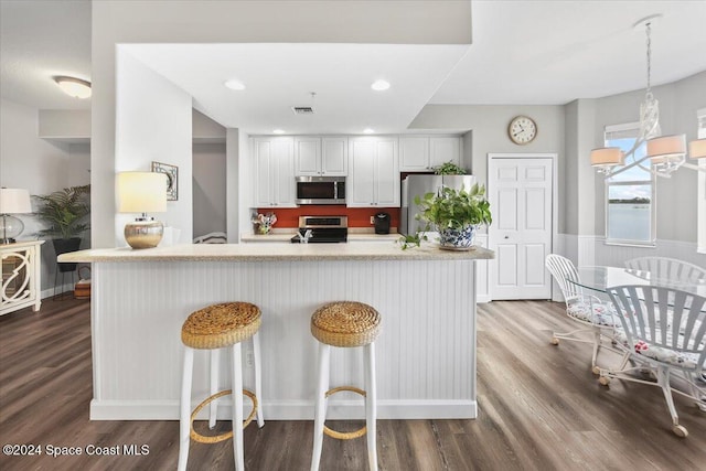 kitchen featuring appliances with stainless steel finishes, a kitchen breakfast bar, dark wood-type flooring, white cabinets, and hanging light fixtures