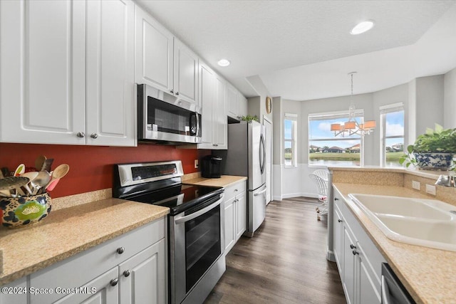 kitchen with stainless steel appliances, sink, white cabinets, a chandelier, and hanging light fixtures