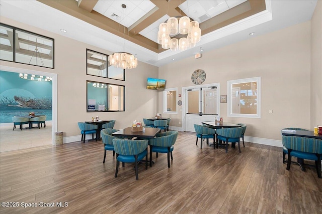 dining space with hardwood / wood-style floors, a towering ceiling, an inviting chandelier, and a raised ceiling