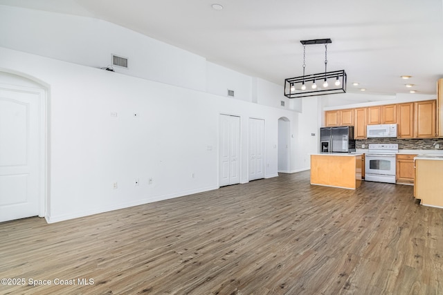 kitchen featuring decorative light fixtures, tasteful backsplash, vaulted ceiling, white appliances, and hardwood / wood-style flooring