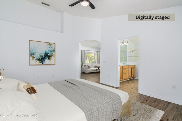 bedroom with ceiling fan with notable chandelier, connected bathroom, and hardwood / wood-style floors