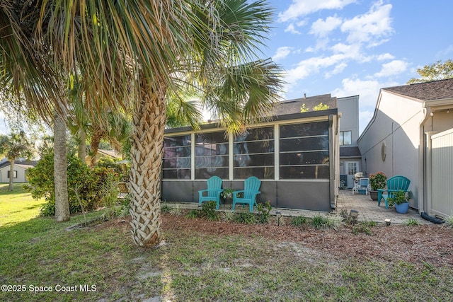 rear view of property featuring a lawn, a sunroom, and a patio