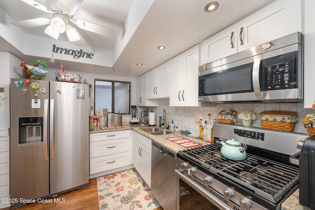 kitchen with white cabinets, sink, light wood-type flooring, appliances with stainless steel finishes, and tasteful backsplash