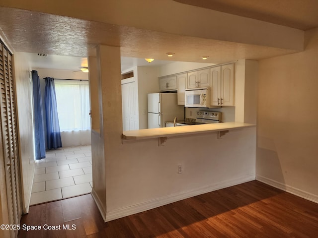 kitchen with a breakfast bar, white appliances, kitchen peninsula, dark hardwood / wood-style flooring, and white cabinetry