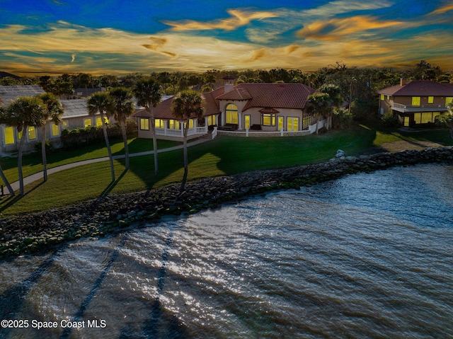 back house at dusk featuring a water view and a yard