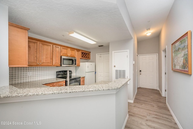 kitchen featuring light stone counters, light hardwood / wood-style flooring, kitchen peninsula, stainless steel appliances, and decorative backsplash