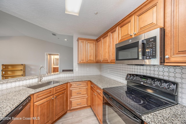 kitchen with sink, vaulted ceiling, stainless steel appliances, and light stone countertops