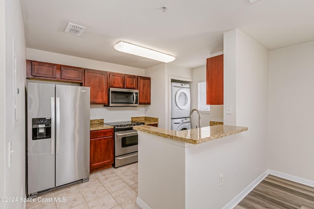 kitchen with kitchen peninsula, appliances with stainless steel finishes, stacked washer and clothes dryer, and sink