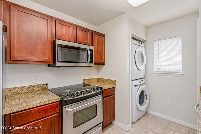 kitchen featuring stacked washer / drying machine, light stone countertops, stainless steel appliances, and light tile patterned floors