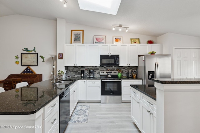 kitchen featuring tasteful backsplash, vaulted ceiling with skylight, sink, black appliances, and dark stone countertops