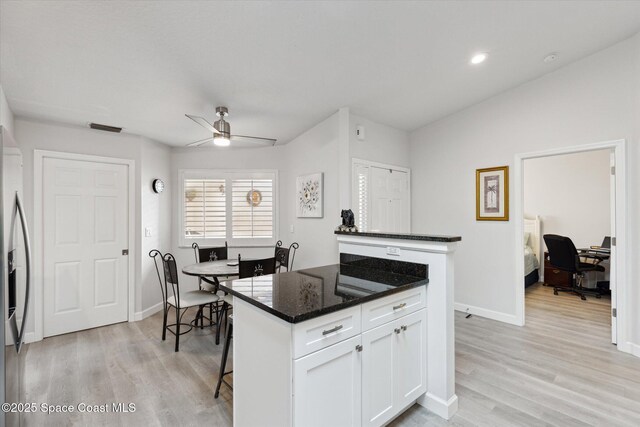 kitchen featuring light hardwood / wood-style flooring, white cabinets, dark stone counters, and a kitchen island