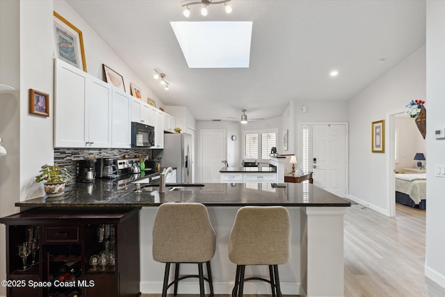 kitchen featuring a skylight, stainless steel appliances, kitchen peninsula, a breakfast bar area, and white cabinets