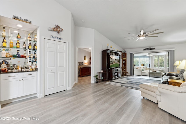 living room with bar, ceiling fan, vaulted ceiling, and light wood-type flooring