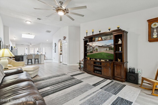 living room with vaulted ceiling with skylight, ceiling fan, and light hardwood / wood-style floors