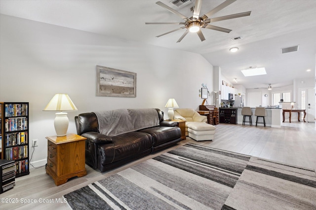 living room with light hardwood / wood-style flooring, ceiling fan, and lofted ceiling with skylight