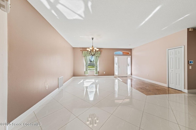 tiled empty room with a textured ceiling and a notable chandelier