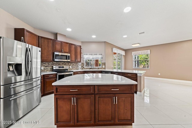 kitchen with a center island, stainless steel appliances, kitchen peninsula, decorative backsplash, and light tile patterned floors