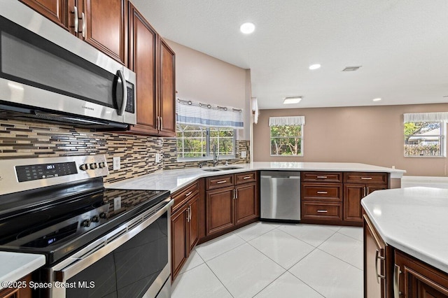 kitchen with sink, kitchen peninsula, decorative backsplash, light tile patterned floors, and appliances with stainless steel finishes