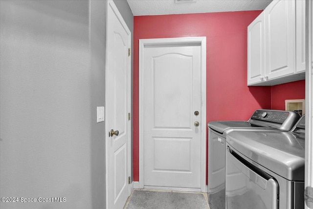 clothes washing area featuring cabinets, a textured ceiling, and washing machine and dryer