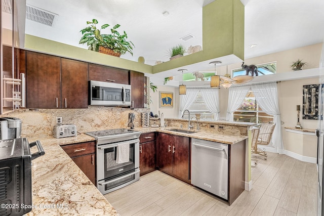 kitchen featuring a high ceiling, sink, light stone counters, kitchen peninsula, and stainless steel appliances